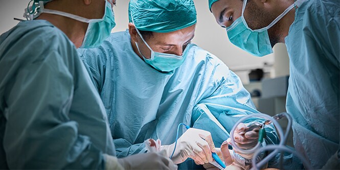Tre chirurghi impiantano una protesi mammaria su una paziente
