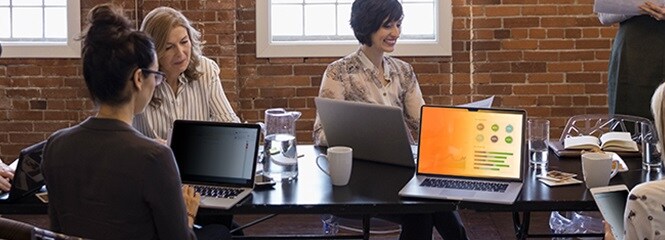Persone che lavorano sedute attorno a un tavolo con laptop che mostrano dati sensibili
