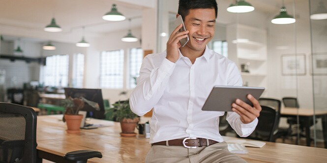 Immagine di un uomo d'affari sorridente che parla al telefono e guarda il tablet.
