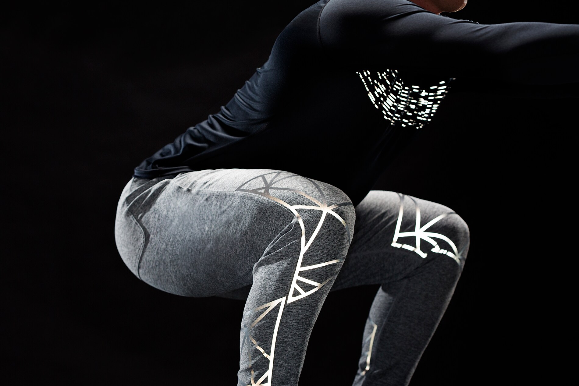 Uomo che esegue una serie di squat con materiale riflettente elastico 3M Scotchlite illuminato che si allunga sulle ginocchia e sul torace