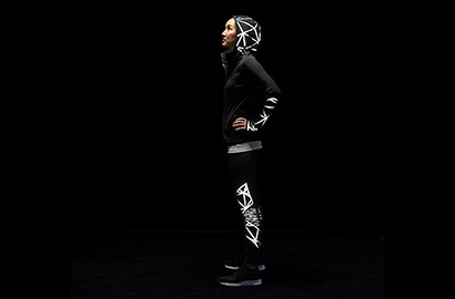 Donna in piedi al buio che indossa giacca e pantaloni illuminati, realizzati con materiale riflettente elastico nero 3M Scotchlite