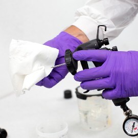 Mani con guanti viola che puliscono l'ago di una pistola spray con un panno bianco