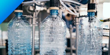 Tre bottiglie di plastica piene di acqua in un impianto di produzione.
