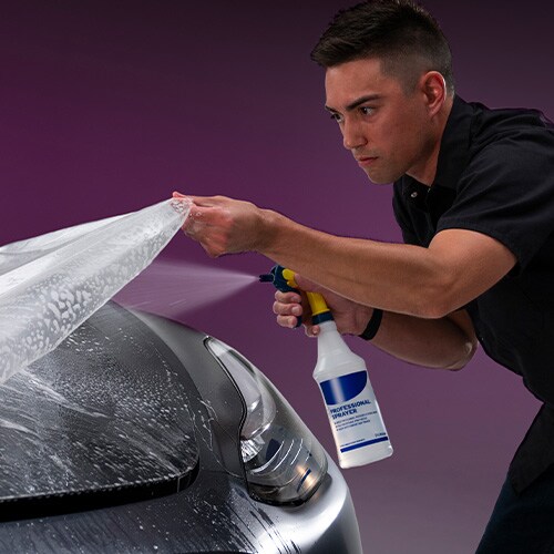 Uomo che spruzza acqua durante l'installazione di protezione vernice sul cofano dell'auto
