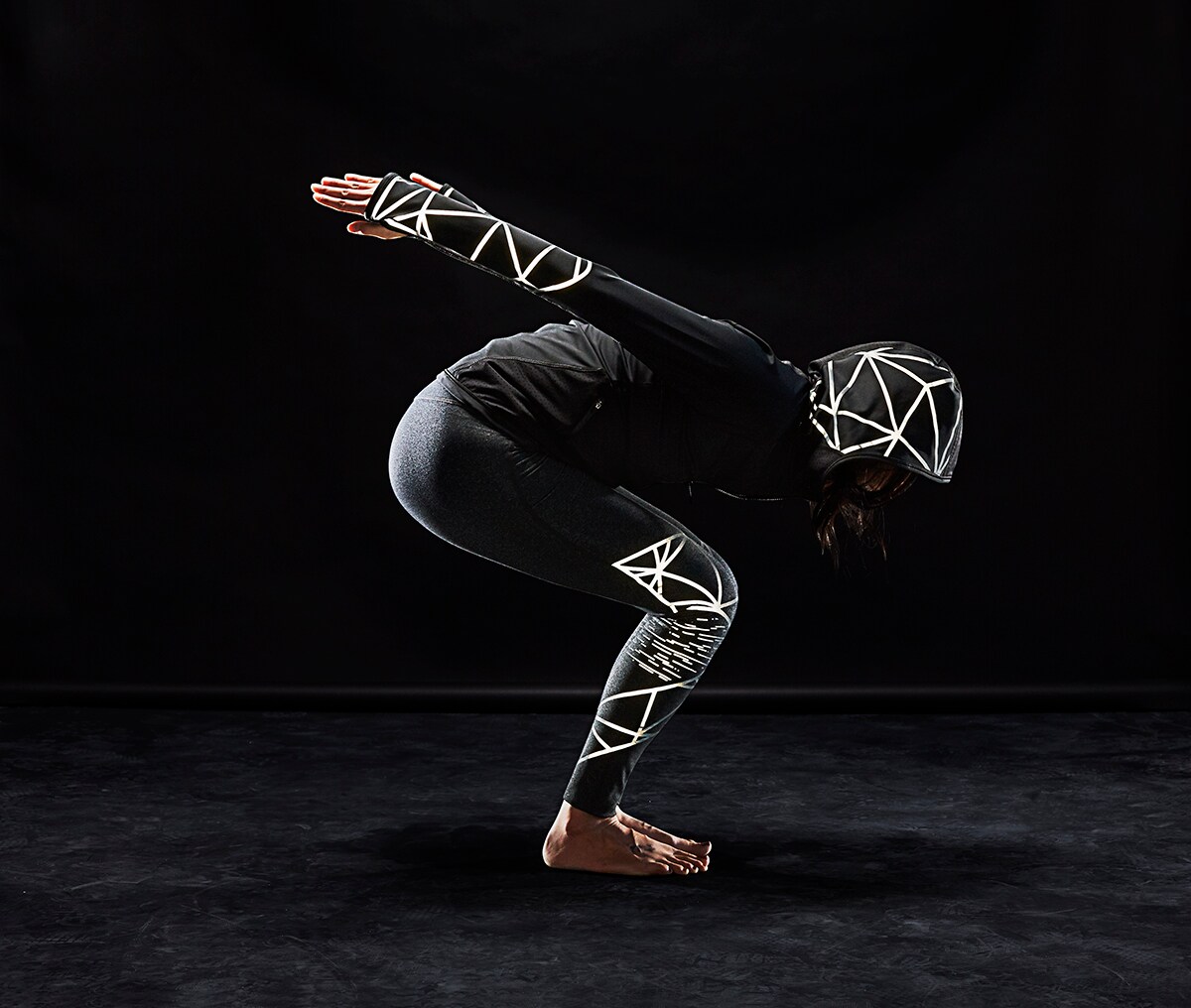 Donna atletica in posizione yoga che indossa abbigliamento tecnico con materiale riflettente elastico nero 3M Scotchlite C790 illuminato