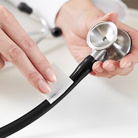 Mani che puliscono il tubo di uno stetoscopio Littmann con una salvietta imbevuta di alcool.