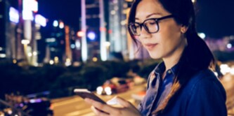 donna che osserva il telefono con sullo sfondo lo skyline della città
