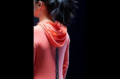 Donna in piedi al buio che indossa una felpa rosa con cappuccio, con strisce di materiale riflettente elastico nero 3M Scotchlite al centro della schiena
