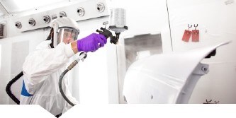 Verniciatore spruzza primer su una parte di auto utilizzando una pistola spray 3M
