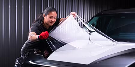 Installatore car wrap che applica la pellicola sul cofano di un veicolo.
