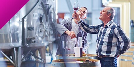Due uomini che osservano un bicchiere di vino in una cantina.
