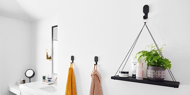 Una parete del bagno con i ganci per cartongesso 3M CLAW™ con appesi pianta e asciugamani.
