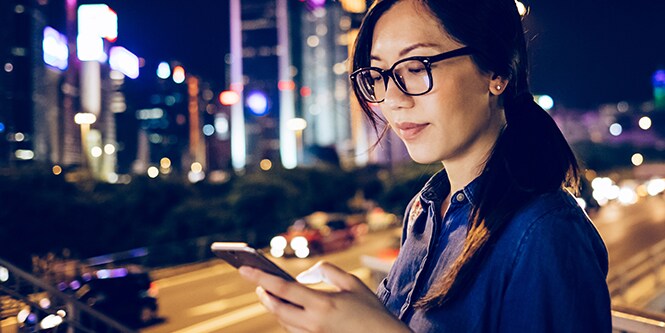 Immagine di una donna che utilizza il suo dispositivo mobile in una città di notte.
