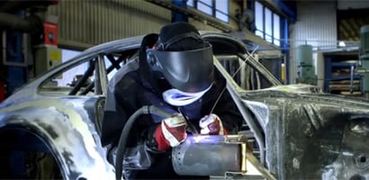 immagine che mostra un saldatore che indossa un dispositivo di protezione, mentre utilizza una torcia di saldatura su una struttura metallica in uno stabilimento di produzione
