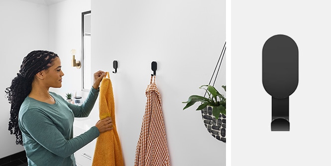 Donna che appende gli asciugamani sui ganci da parete neri 3M CLAW™ in bagno
