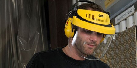 uomo che indossa una visiera con cuffie auricolari che lavora in un ambiente industriale
