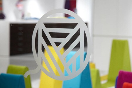 Finestra in vetro trasparente con logo in vetro smerigliato con forme colorate dietro.
