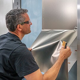 Uomo che installa la finitura 3M DINOC in argento metallizzato sulla porta dell'ascensore