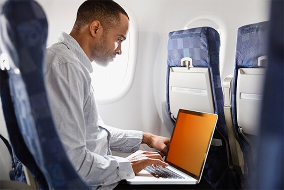Uomo al lavoro su un computer portatile con filtro privacy oro su un aeroplano