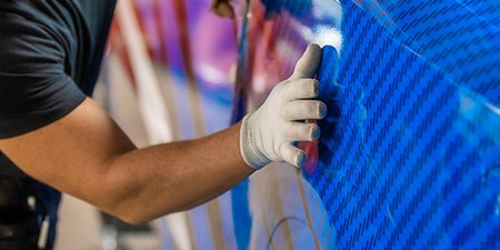 Persona che applica una pellicola da wrapping blu ad un veicolo
