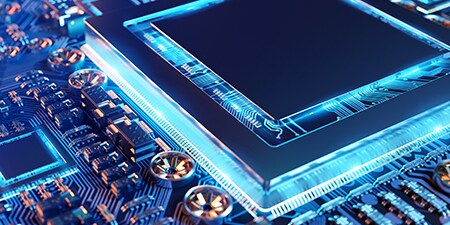 Primo piano di una scheda circuiti elettronica con un microchip al centro, illuminata da un bagliore blu 
