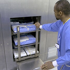 Un operatore della centrale di sterilizzazione spinge il carrello dello strumento nell'autoclave