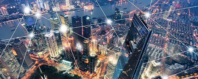 Vista di uno skyline urbano, sorvolato da una rete geometrica di punti luce collegati da linee rette.
