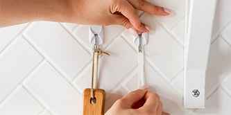 Persona che mostra come utilizzare i ganci e le strisce Command™ per una migliore organizzazione.
