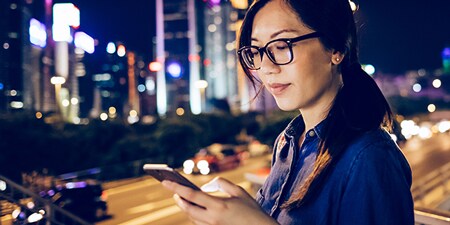 Donna che usa il suo dispositivo mobile in una città di notte.
