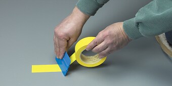 Un'immagine contenente una persona che attacca il nastro giallo sul pavimento
