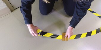 Un'immagine contenente una persona che attacca il nastro giallo-nero sul pavimento

