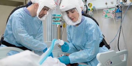 Immagine che mostra due operatori sanitari che indossano DPI mentre assistono un paziente
