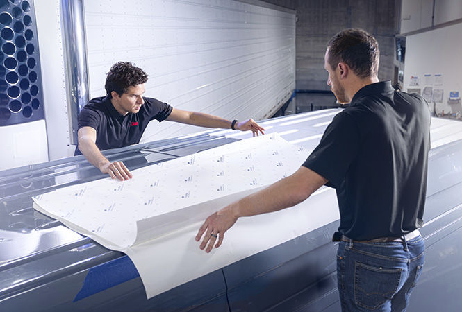 Tecnici che applicano la pellicola 3M sul tetto di un veicolo all’interno di un’officina.
