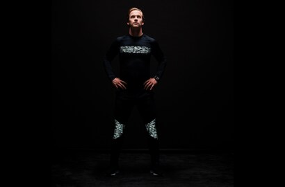 Uomo in piedi al buio che indossa maglia e pantaloni illuminati, realizzati con materiale riflettente elastico nero 3M Scotchlite