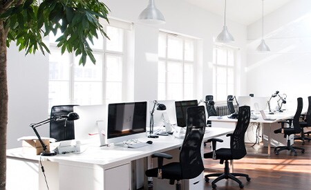 Spazio ufficio moderno e bianco, a pianta aperta, con pareti di finestre e luce naturale che splende all'interno
