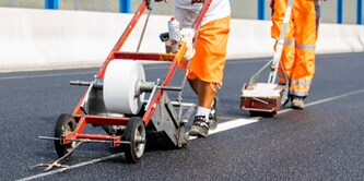 Persone che applicano un nastro adesivo per segnaletica orizzontale su una nuova strada

