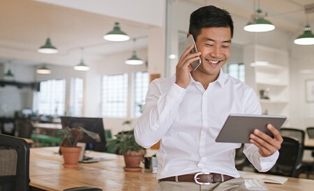 Immagine di un uomo d'affari sorridente che parla al telefono e guarda il tablet.
