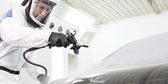 Tecnico verniciatore che spruzza vernice su un veicolo.
