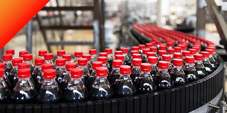 Centinaia di bottiglie di plastica di bibite analcoliche scure su un nastro trasportatore.
