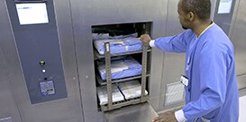 Un operatore della centrale di sterilizzazione spinge il carrello dello strumento nell'autoclave
