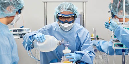 immagine che mostra tre operatori sanitari che indossano DPI mentre assistono un paziente
