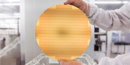 Mani che tengono un wafer semiconduttori color oro
