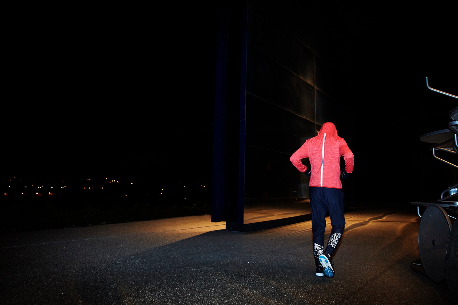 Materiale riflettente elastico nero illuminato sulla schiena di un uomo che cammina accanto a una parete di specchi, di notte