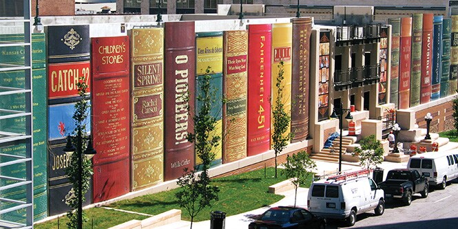 Immagine esterna di una biblioteca avvolta in una pellicola grafica stampata in modo da sembrare libri giganti allineati.
